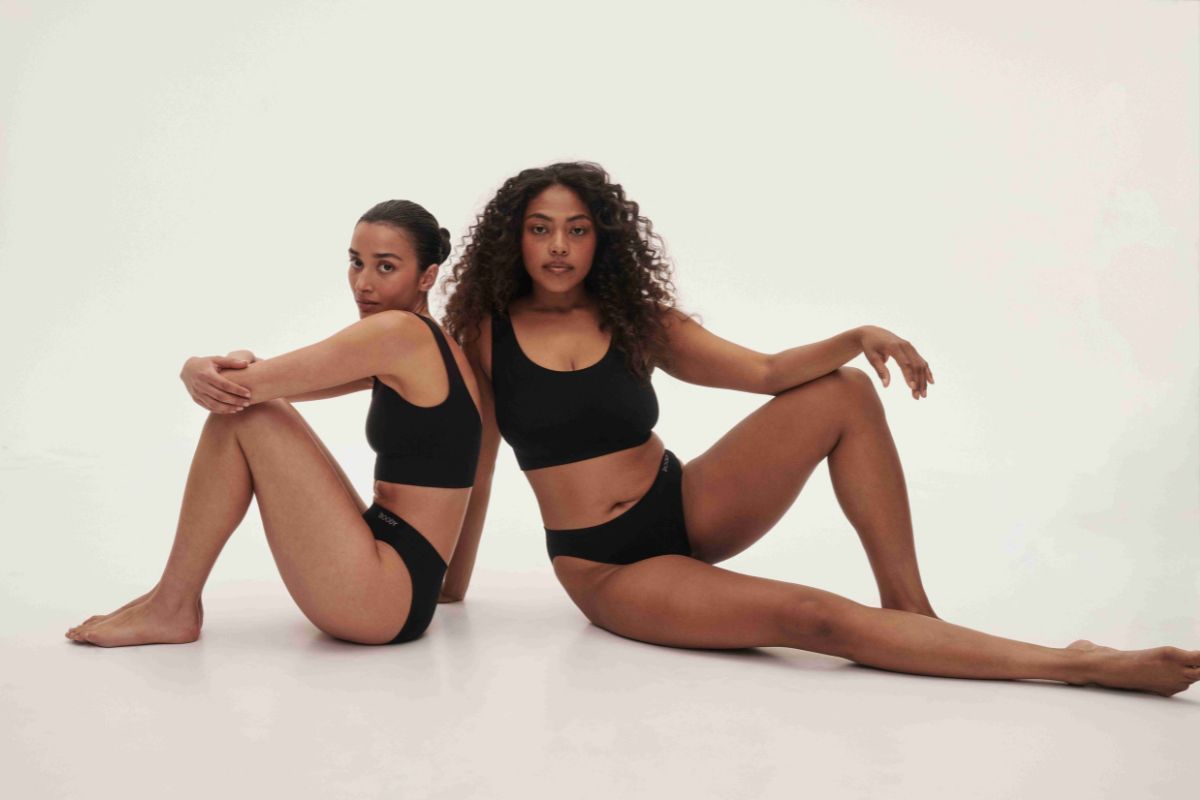 Two women in black seamless underwear and crop bras posing in a neutral studio setting.