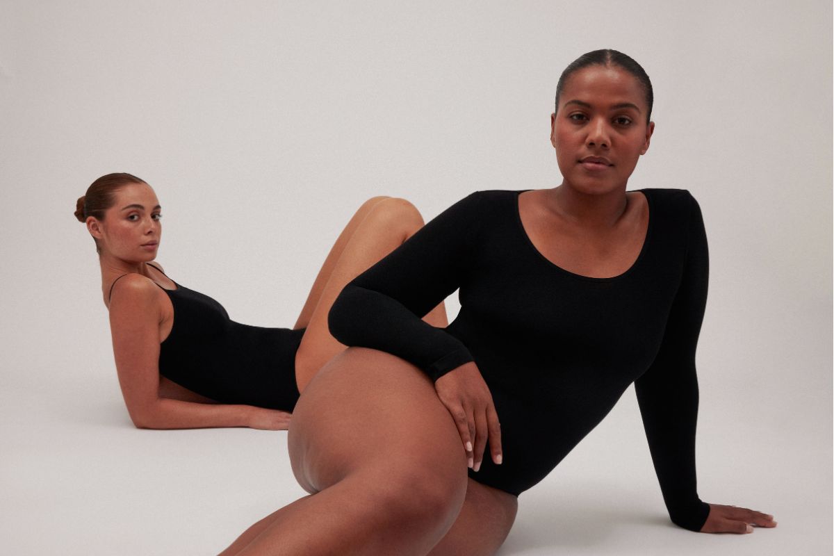 Two models wearing black long sleeve bodysuits against a neutral studio backdrop.