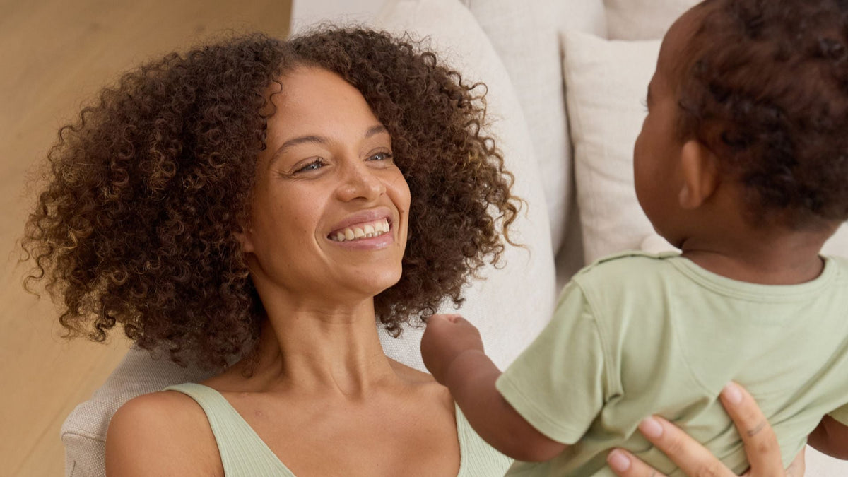 Smiling mother holding her baby while they wear soft green clothing.
