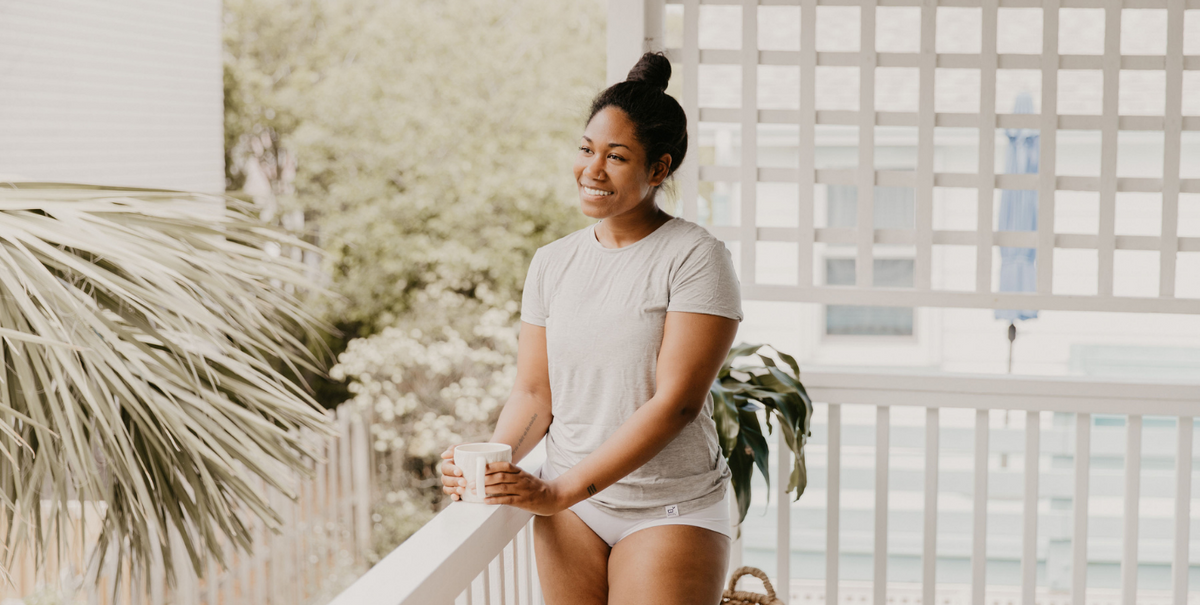 Happy young woman standing on her balcony with a cup of coffee, wearing bamboo viscose T-shirt
